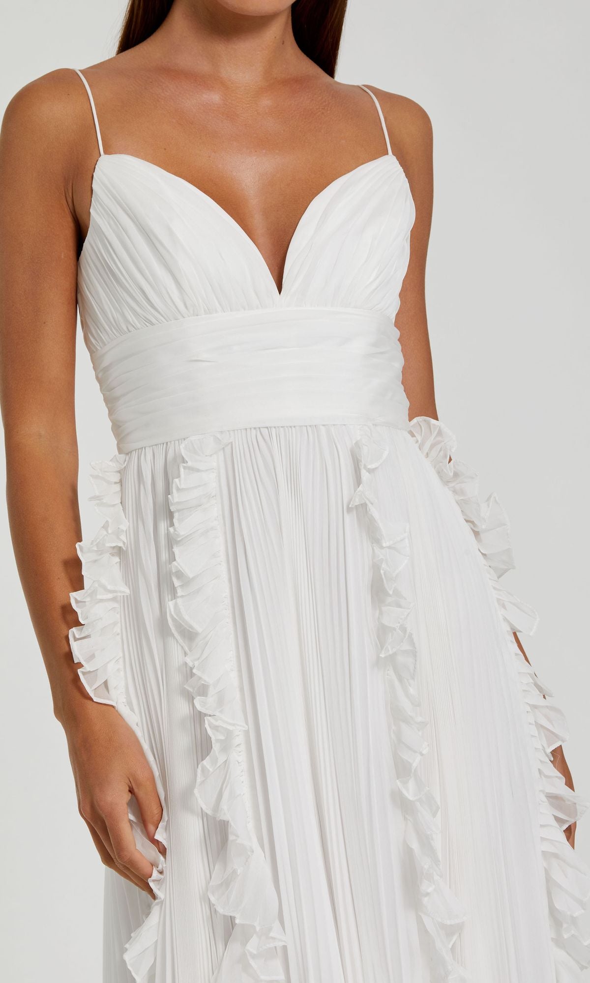 A woman wears the Ruffled Long White Formal Dress 49533, a stunning sleeveless gown with thin straps, a deep V-neckline, ruched waist, and ruffle details—perfect for special occasions.